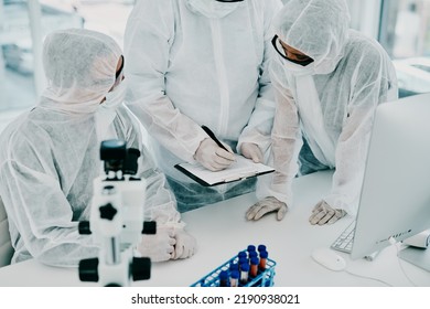 Team Of Scientists, Pathologists And Doctors In Hazmat Suits Discussing Forensic Research And Plans In A Lab. Medical Experts Working On Tests, Experiments And Drug Trial To Develop Cure For Disease