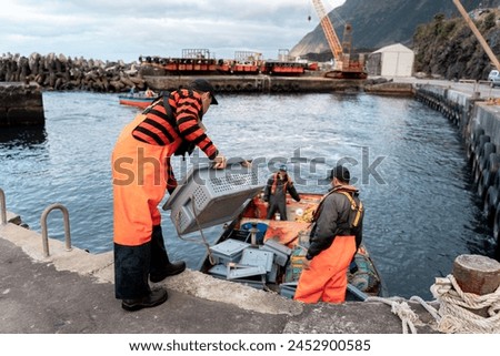 Team of several fishermen unloading crates of freshly caught lobsters at the port in a cloudy cold day