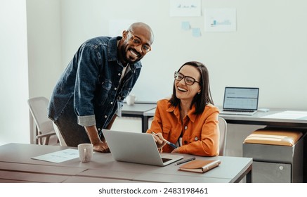 Team of smiling coworkers working together on a laptop in a bright, modern office setting, demonstrating teamwork and collaboration.