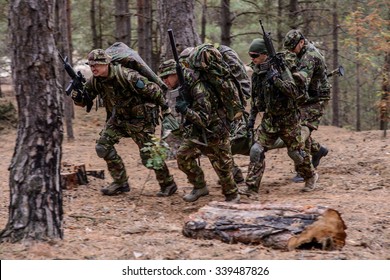 Team Of Soldiers Evacuate Wounded Soldier On A Stretcher From Battlefield In Forest/Evacuation Of Wounded Soldier