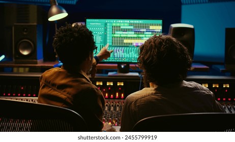 Team of sound engineers working on recording and editing tracks in professional studio control room, collaborating on mix and master audio files. Musician and technician pressing sliders. Camera B. - Powered by Shutterstock