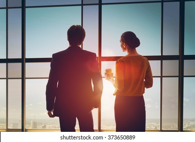 Team Of Successful Business People. Two Businessmen Resting And Talking In The Office. Man And Woman Look At The City From The Window Of The Business Center.
