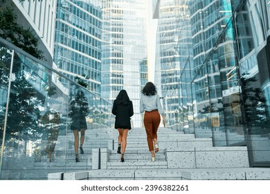 A team of successful business women of different races walking up the steps discussing strategy, rear view. Various women walk along the street against the backdrop of buildings. - Powered by Shutterstock