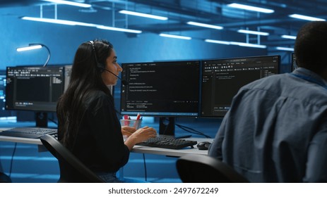Team of IT support experts working together, supervising server rows in computer network security data center. Woman next to colleagues talking in headphones mic while overseeing supercomputers