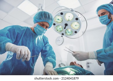 Team surgeons are performing an operation using medical instruments, in a modern operating room