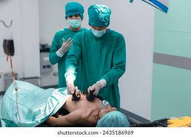 Team of surgery doctor using defibrillator pump chest heart patient to save life while medical surgery in operating room. Defibrillator in surgeon specialist hand. - Powered by Shutterstock