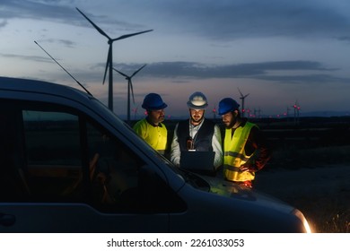 Team of technicians and engineer working in wind turbine farm at night, planing renewable energy ecology project - Powered by Shutterstock