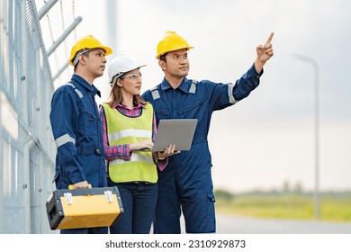 A team of three Asian female mechanics and engineers wearing maintenance suits and vests. point to destination working on tablet near the industrial plant holding a toolbox and wearing a helmet