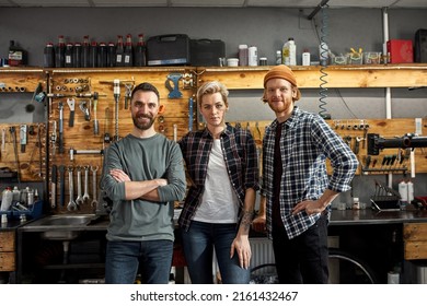 Team Of Three Cycling Workers Posing And Looking At Camera At Workplace In Modern Bicycle Workshop. Young Caucasian Men And Woman. Friendship. Teamwork. Bike Service, Repair And Upgrade