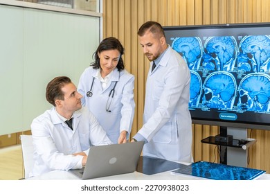 Team of three doctors discusses the results of an MRI scan of the patient's head in the consulting room of modern hospital, physician discussing about treatment for patient looking in laptop - Shutterstock ID 2270938023