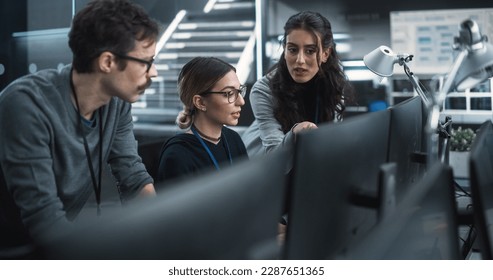 Team of Three Talented Young Software Engineers Use Computer to Discuss a Technological Project in Modern Industrial Office. Group of Male and Female Scientists Work in Research and Development Center - Powered by Shutterstock