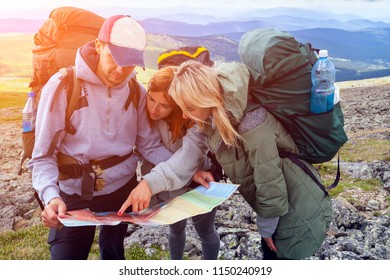 A team of travelers from two women and men with backpacks orient themselves to the terrain, study maps and navigate the route through the mountains. Travel Lifestyle and survival concept rear view.  - Powered by Shutterstock