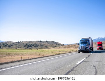 Team of two big rigs industrial professional semi trucks tractors transporting cargo in dry van semi trailers driving side by side on the straight highway road along the bald hills in California