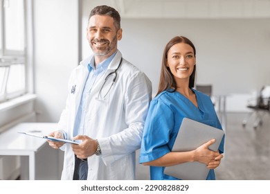 Team of two professional doctors working together in clinic, man posing with digital tablet, woman with clipboard, looking and smiling at camera. Healthcare and medicine concept - Powered by Shutterstock