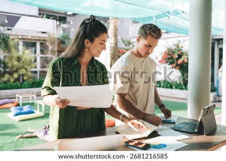 Team of two reviewing graphs and notes during a strategy session, integrating mobile devices and printed documents to align ideas in a productive digital workspace.