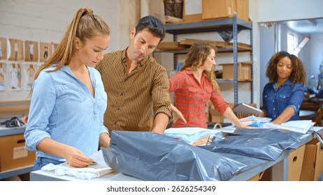 Team Using Digital Tablet Working In Distribution Warehouse Packing Clothes For Customer Delivery