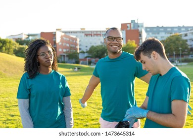 Team Volunteers Enjoying Work Break And Chatting. Men And Woman Wearing Uniforms And Gloves Standing On City Lawn And Talking. Volunteer Team Concept