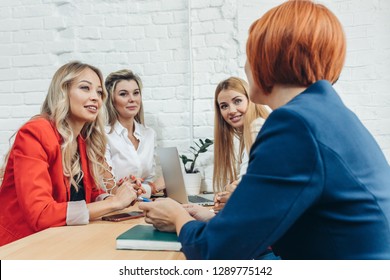 Team Work Process. Multiracial Group Of Young Women Collaborating In Open Space Office. Red-haired Mentor Coach Speaking To Young People, Teaching Audience At Training Seminar.