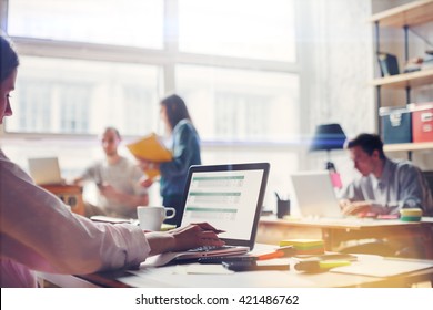 Team work process. Young business crew in big loft office. Laptop with graph, analysing marketing. Film effect, blurry background, lens flare effect - Shutterstock ID 421486762