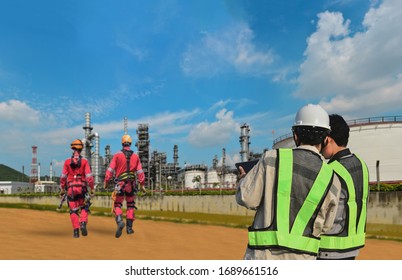 Team Worker In Oil Refinery Discussion For Inspection By Hand Holding Tablet On Power Plant With Refinery Plant Structure And Two Worker Wearing Safety Harness Walking In Background.