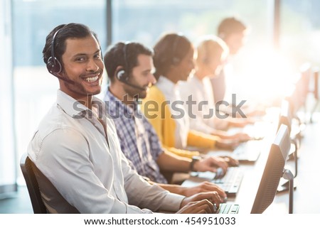 Team working on computer with headset while a colleague smiling at camera in the office