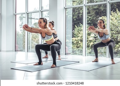 Team Yoga Class Female Trainer Leading Group In Fitness Squat Calorie Burning Exercise. Side View