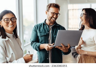 Team of young business people having a meeting in an office. Group of happy professionals standing together with a laptop. - Powered by Shutterstock