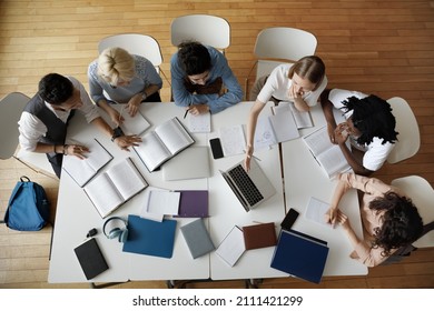 Team of young college students working on study project in university library, using laptop, writing notes at table with books, sharing learning tasks. Top aerial view - Shutterstock ID 2111421299