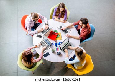 Team Of A Young Coworkers Dressed Casually Working Together With Laptops Sitting At The Round Table In The Office, View From Above