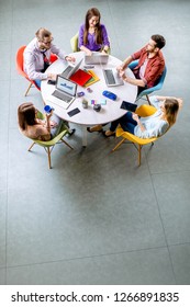 Team Of A Young Coworkers Dressed Casually Working Together With Laptops Sitting At The Round Table In The Office, View From Above