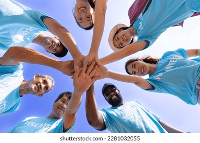 Team of young and diversity volunteer worker group enjoy charitable social work outdoor together in saving environment project wearing blue t-shirt while joining hand in power assemble unity