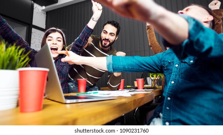 Team Of Young Employees Looking At The Data On The Laptop, Indoor Shot Of Happy Reaction To Successful Result While Working In Dark Green Office