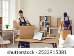 Team of young happy cheerful professional workers of moving service in overalls carrying, delivering and unpacking cardboard boxes in new office. Move, moving day and relocation concept.