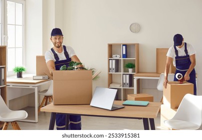 Team of young happy cheerful professional workers of moving service in overalls carrying, delivering and unpacking cardboard boxes in new office. Move, moving day and relocation concept. - Powered by Shutterstock