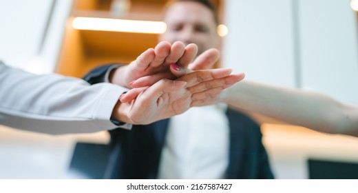 Team Of Young Male And Female Employees Stacking Hands On Top Of Each Others To Depict Unity And Harmony Amongst Colleagues For Project And Positive Work Environment In Modern Office