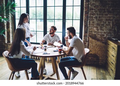 Team of young male and female multiracial designers gathering around table and discussing project details during brainstorming session in loft office - Powered by Shutterstock