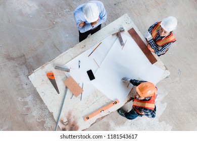 Team of young man and woman engineer and architects working, meeting, discussing, designing, planing, measuring layout of building blueprints in construction site floor at factory. Top view.