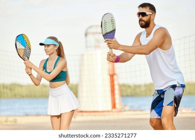 Team. Young man and woman playing paddle tennis on beach on warm summer day near river. Outdoor activity. Concept of sport, leisure time, active lifestyle, hobby, game, summertime, ad - Powered by Shutterstock