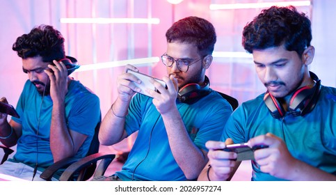 Team Of Young Professional Gamers Playing Live Video Game On Mobile Phone By Talking On Headphones At Esports League