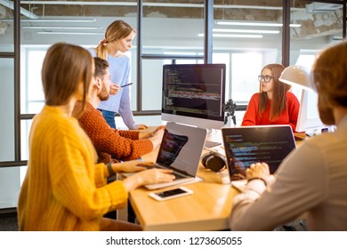 Team of a young programmers dressed casually working on computer code sitting in the modern office interior