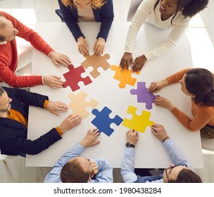 Team of young and senior employees sitting in circle around office table putting jigsaw puzzle together as metaphor for teamwork and looking for working business solutions. Square format, high angle - Shutterstock ID 1980438284
