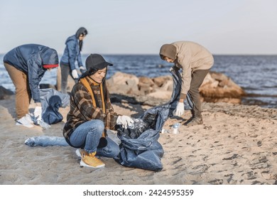 Team of young volunteers are picking up plastic on a beach. Littering prevention, saving the nature. Environmental protection from contamination and plastic pollution - Powered by Shutterstock