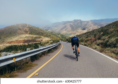 Teammates Cycling, Cyclist Bunch Riding Together And Descending Narrow One Lane Road Into The Fog In Marin County, Just North Of San Francisco, California.