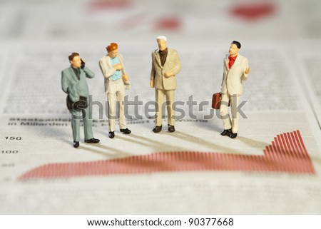 Teamwork And Analysis, four miniature businessmen standing analysing performance above a red bar graph.