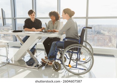 Teamwork brainstorm. Diverse multiracial colleagues woman in chair for people with disability working together. Group of people sitting in creative office discussing business. Young professional team