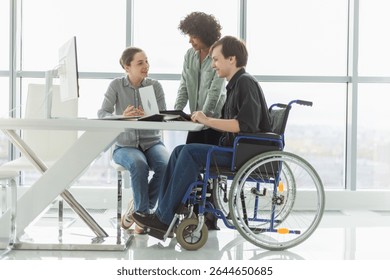 Teamwork brainstorm. Diverse multiracial colleagues man in chair for people with disability working together. Group of people sitting in creative office discussing business. Young professional team