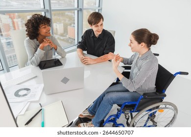 Teamwork brainstorm. Diverse multiracial colleagues woman in chair for people with disability working together. Group of people sitting in creative office discussing business. Young professional team