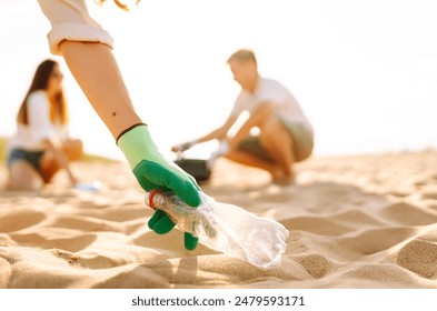 Teamwork cleaning plastic on the beach. Volunteers collect trash in a trash bag. Plastic pollution and environmental problem concept. Voluntary cleaning of nature from plastic. Greening the planet. - Powered by Shutterstock