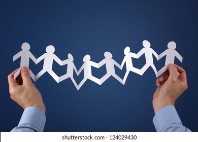 Teamwork concept with paper chain group of people holding hands held over blue background