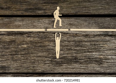 Teamwork concept using paper cut outs of men with one holding up a bridge in a gap so that the other can walk across over rustic wood with copy space.